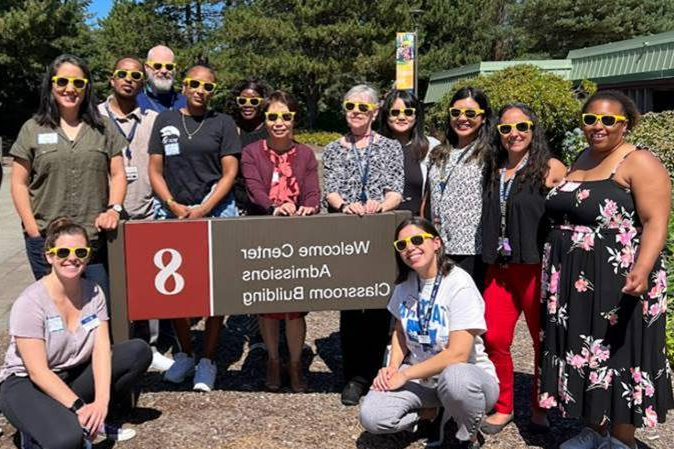 a large group of people in sunglasses standing around TCC's Building 8 Welcome Center sign 
