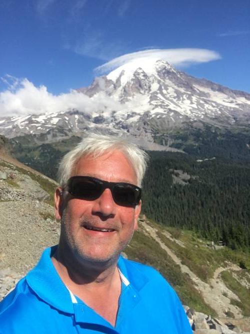 一个白发男子戴着墨镜站在山前的照片. 